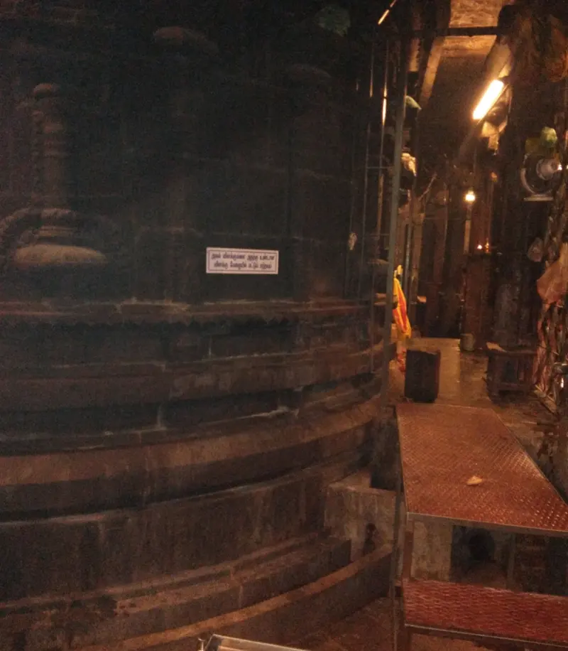 A dark, rounded stone wall with stepped bands beside a lit corridor and a red metal platform