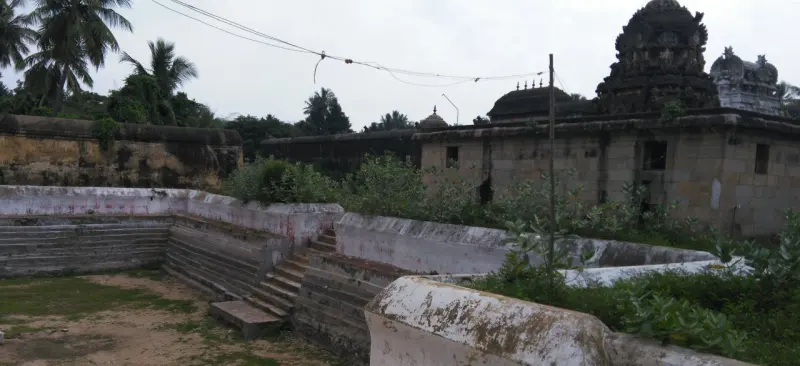 A dry stone tank with steps beside the temple wall, with the shrine towers rising behind.