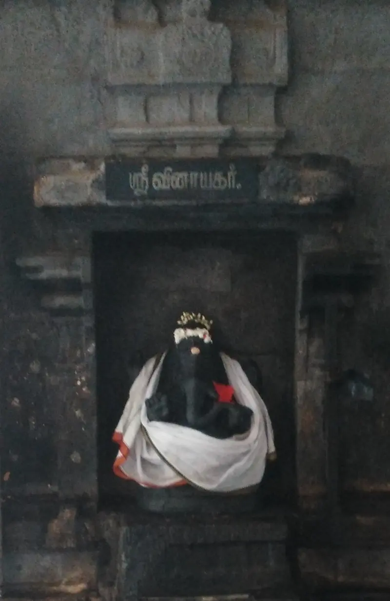 A dark Vinayakar idol with flowers and white cloth in a stone niche