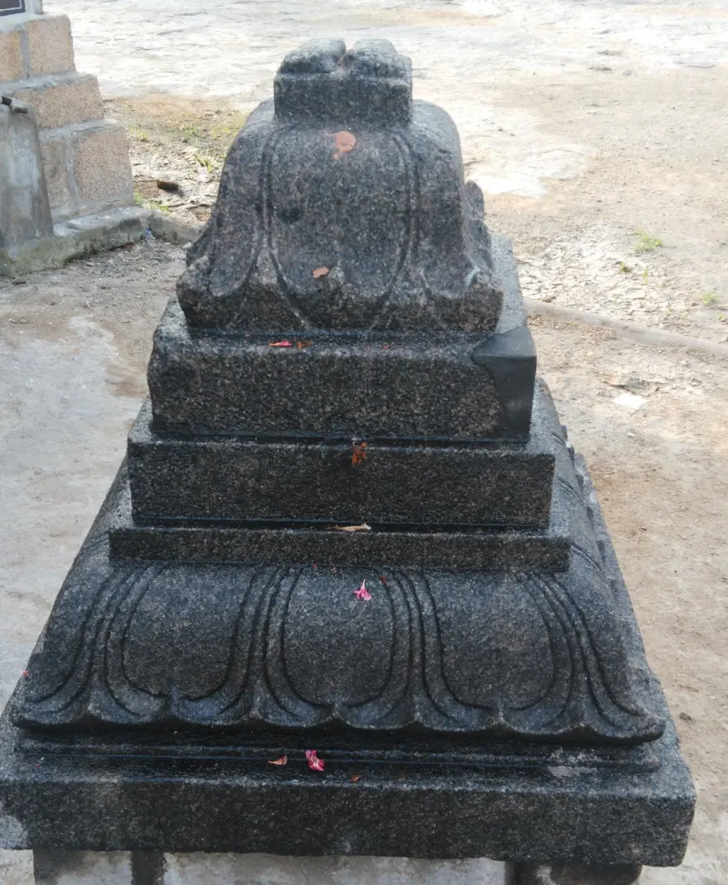 A stepped black stone pedestal with lotus-petal carving and a few petals on it