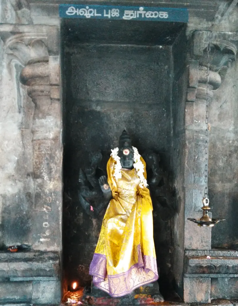 A goddess idol in a yellow saree inside a stone niche