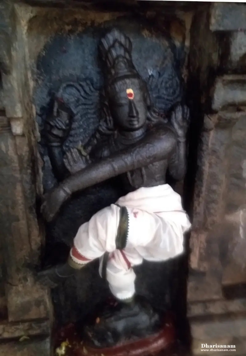 A dark stone idol in a niche with one leg raised and an arm stretched across the body