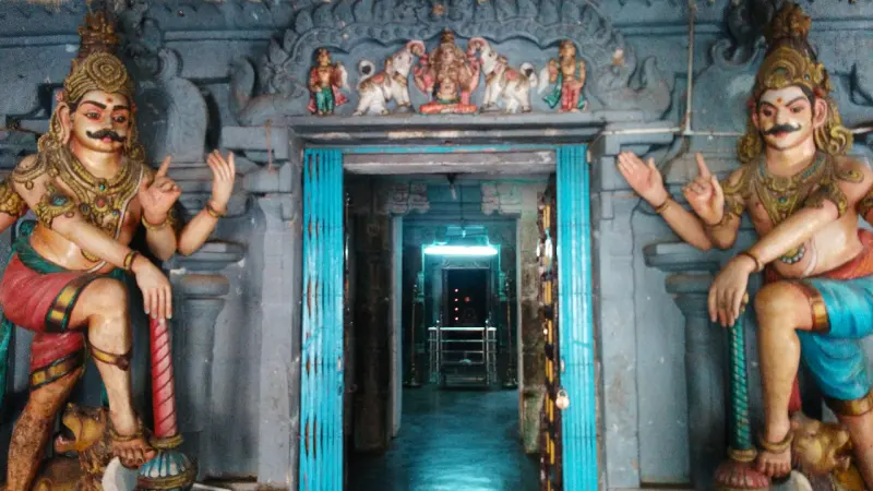 Two painted guardian figures with raised hands flank a blue door; a small figure panel sits above the lintel.