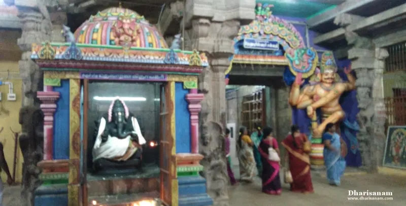 A dark Vinayakar idol in a small painted shrine, with a large guardian figure and visitors nearby