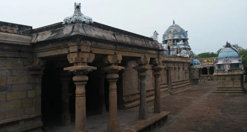 Stone corridor with square pillars; two blue-domed shrine towers appear in the distance