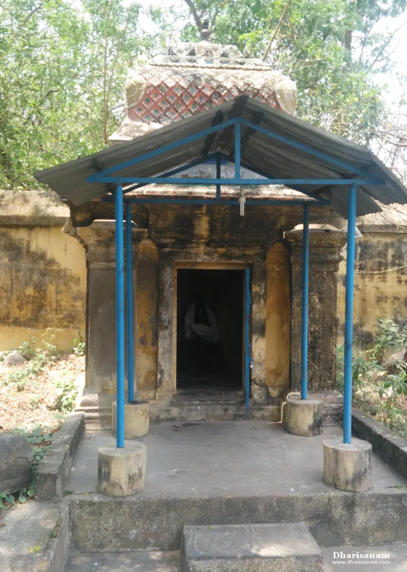 A small stone shrine with a patterned dome, sheltered by a blue-framed tin roof.