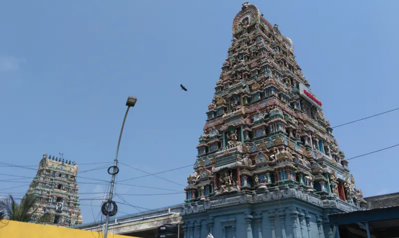 A tall, colourfully painted gopuram against a blue sky, with a smaller tower at the left.