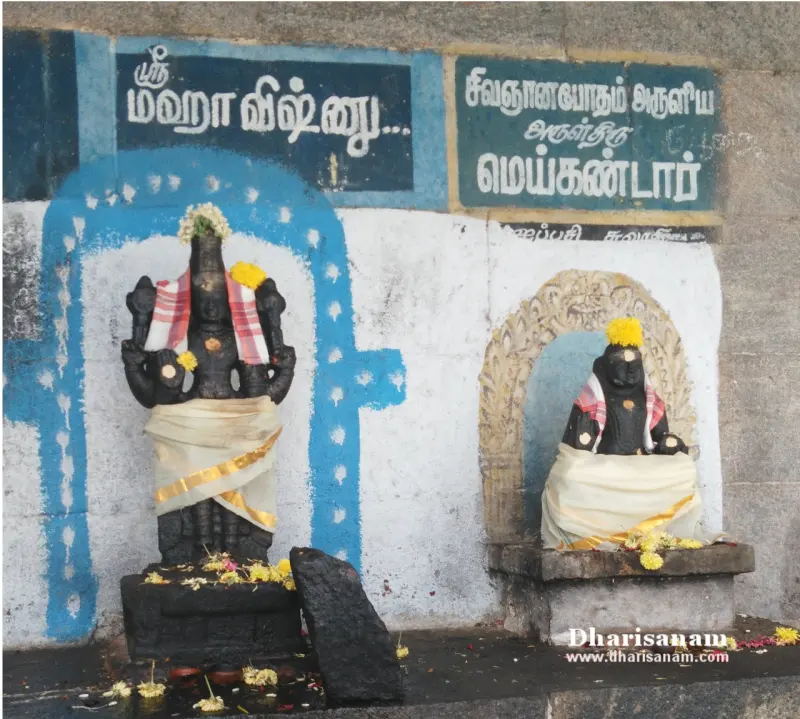 Two black stone idols in cloths with flowers, with Tamil name boards above them