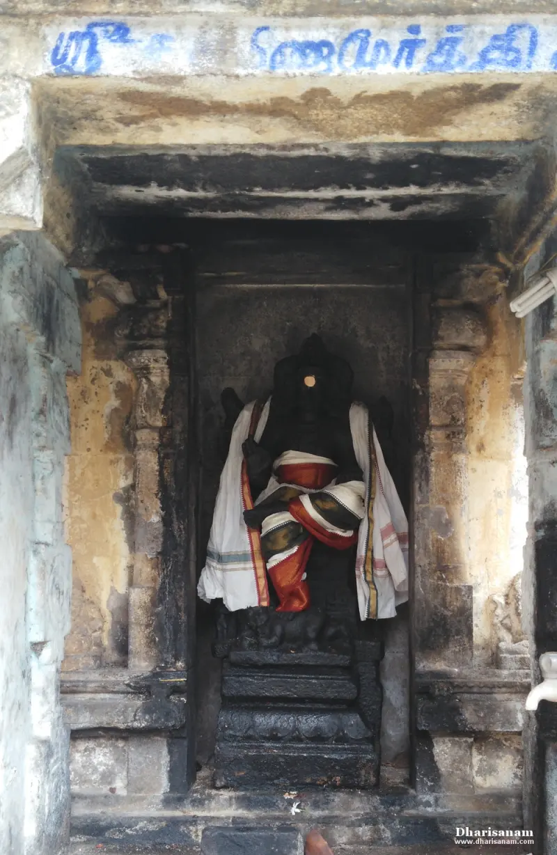 A dark seated Vinayakar idol dressed in white and red cloth, inside a stone niche