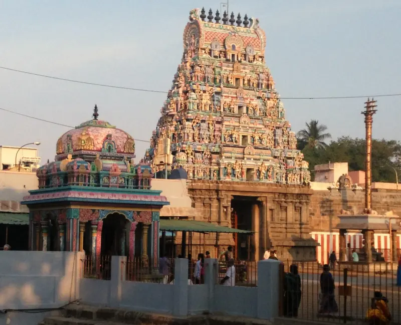 A tower covered in painted figures beside a small pillared shrine with a domed roof and a flag post