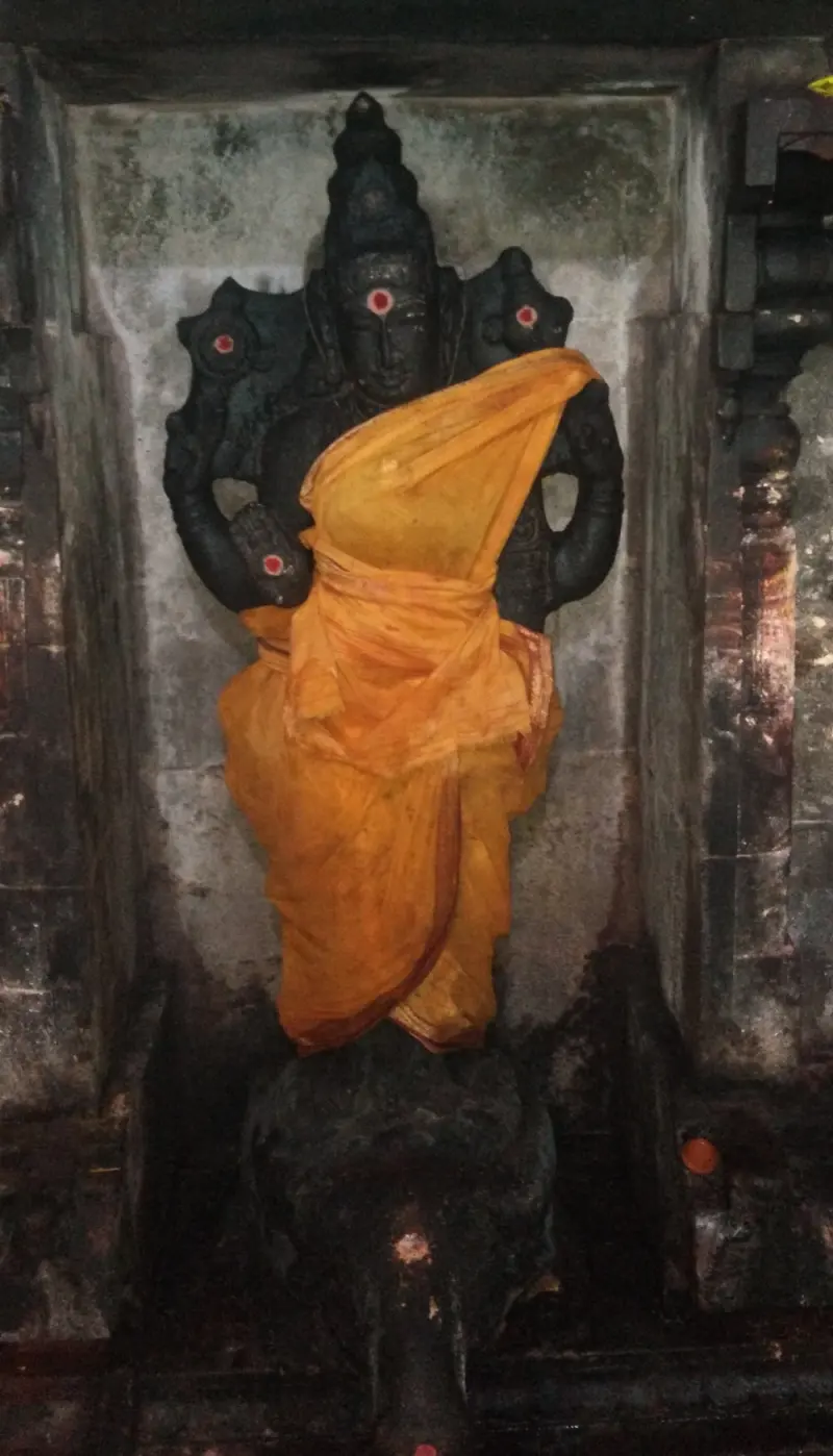 A dark standing figure in a niche, wrapped in an orange cloth