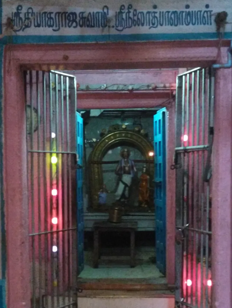 A pink-framed shrine with open grilles; a board above names Thiyagaraja and Neelothbalambal, and idols stand within.