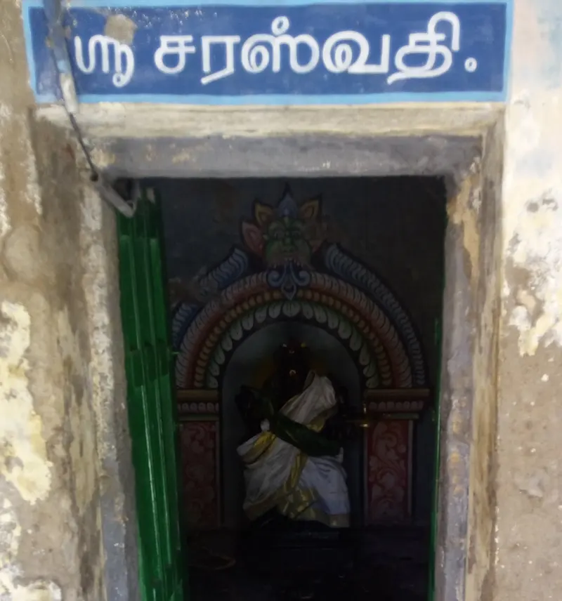Small doorway under a blue Tamil name board, with a dressed image in a painted arch inside