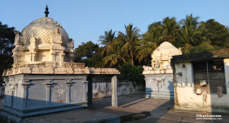 Two small shrines with domed roofs standing in a paved courtyard in evening light, a stone wall behind