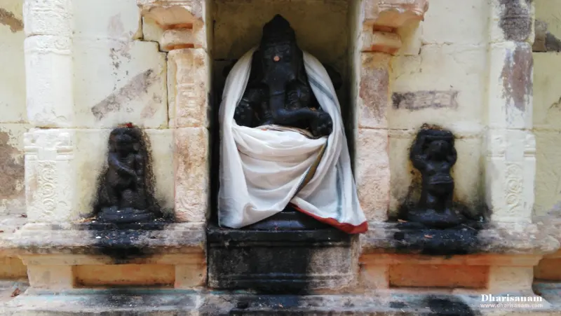 A dark Vinayakar wrapped in white cloth, with small idols on either side