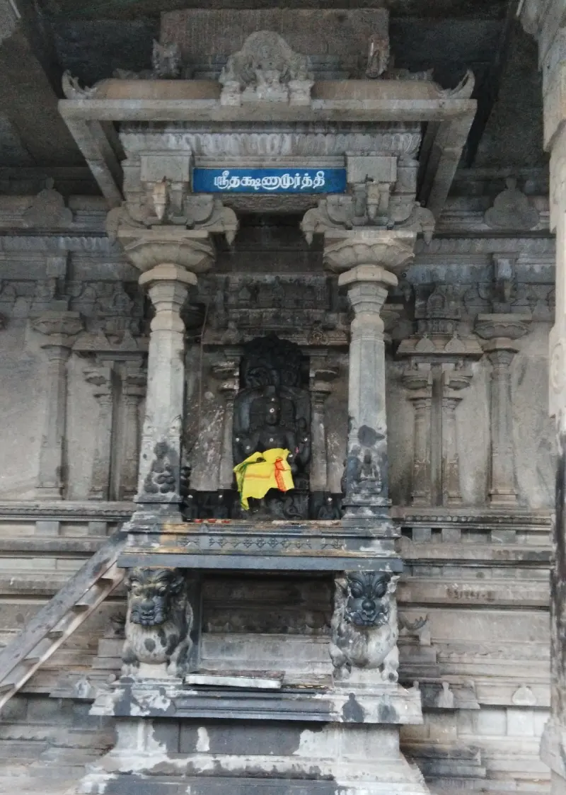 Carved stone niche with a dark seated figure under a Tamil name board