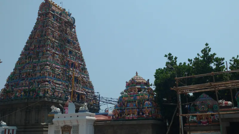 A tall painted tower on the left and a smaller domed shrine tower beside trees and scaffolding.