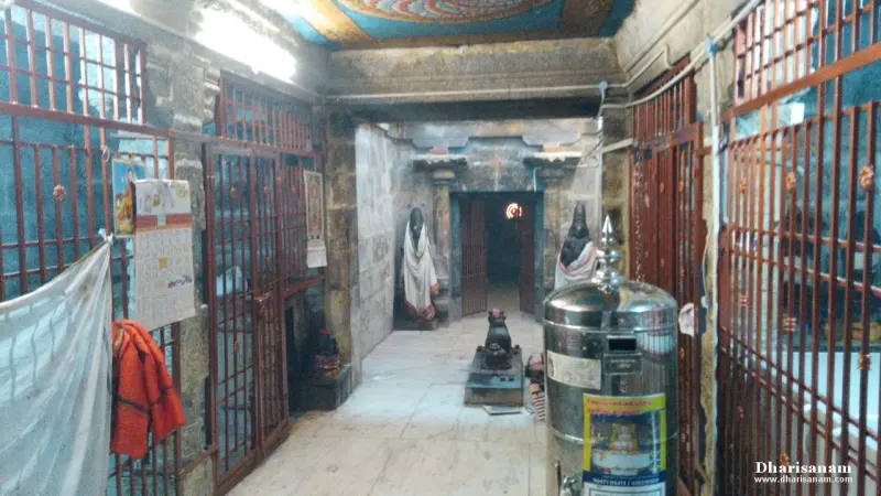 A stone corridor with iron grilles, a small Nandi in the centre and two standing figures at the far end