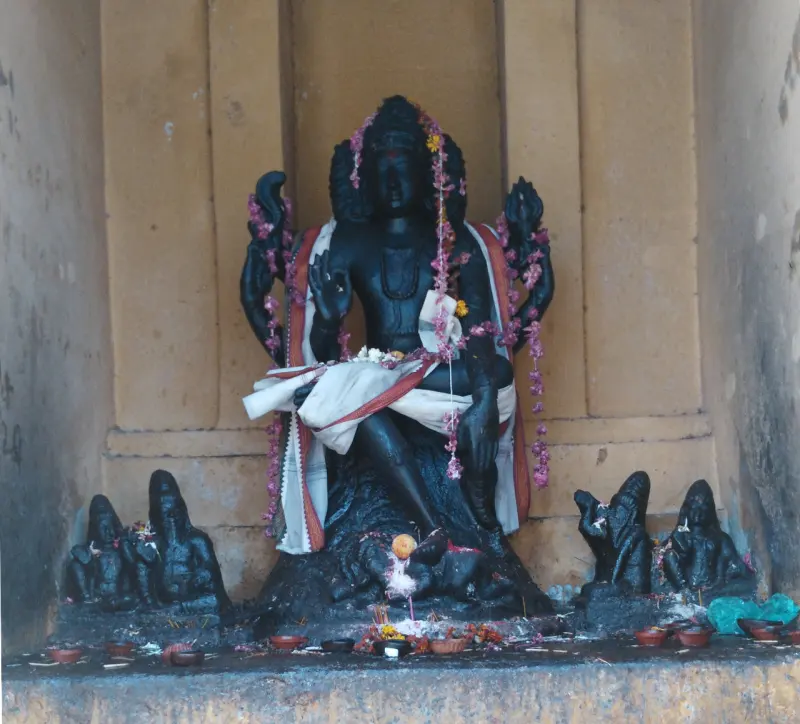 A garlanded black stone deity seated in a niche, with small figures at its feet