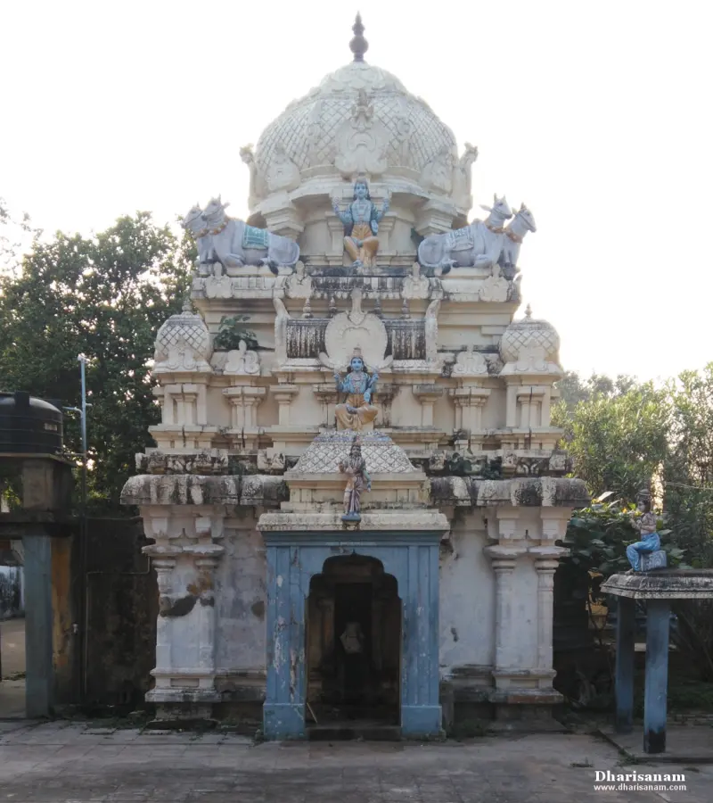 A white shrine tower with painted figures and bulls on its tiers, and a small blue entrance below