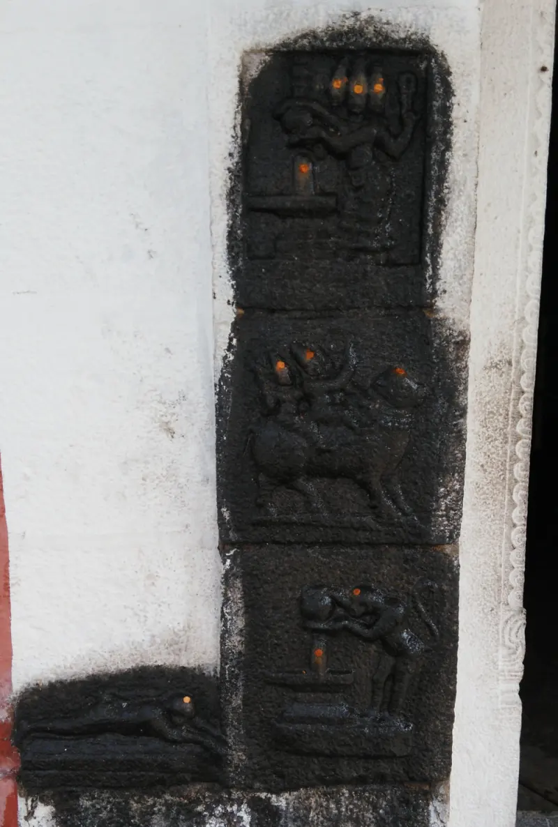 Three dark stone relief panels beside a doorway, showing figures at a lingam and an animal