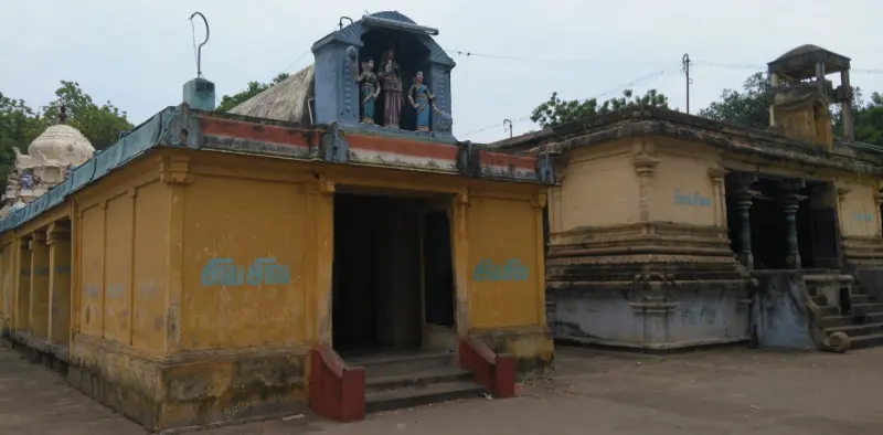 A yellow-walled shrine with steps and painted statues on the roof, a white vimana behind
