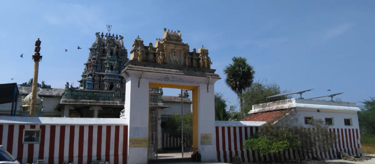 White entrance gate with yellow trim, striped walls and a sculpted tower rising behind