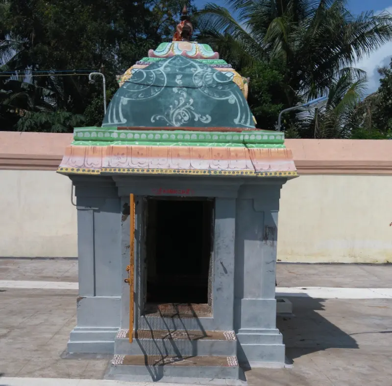 A small grey shrine with a green dome and an open doorway, standing before the compound wall