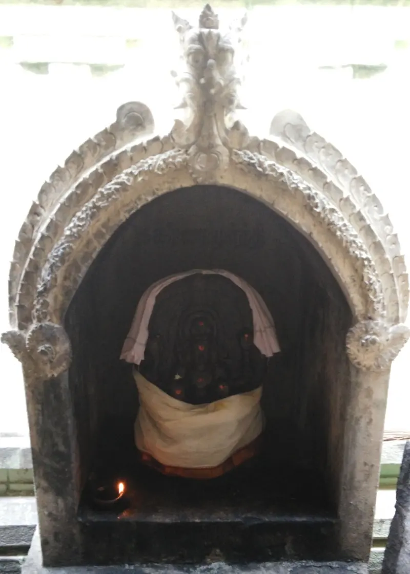 An arched stone niche holding a dark idol draped in white cloth, with a small lamp burning beside it