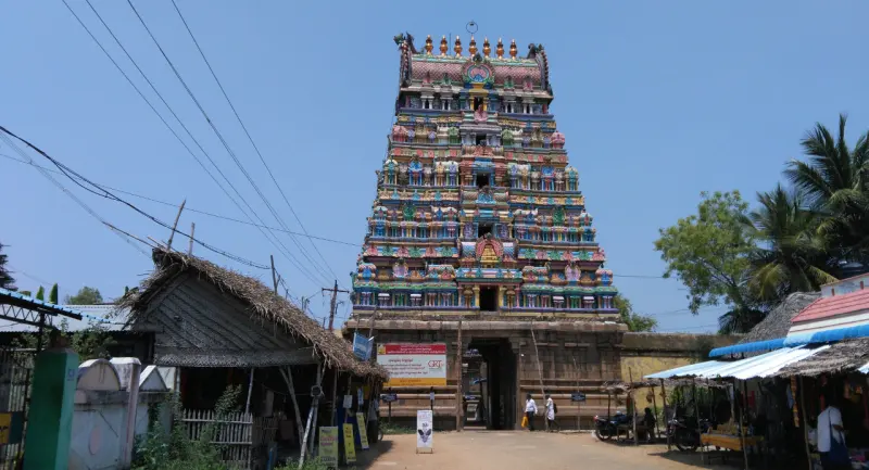 Front view of the tall, tiered and brightly painted Rajagopuram above the gateway, with shops on both sides