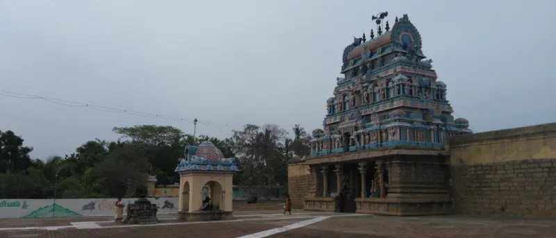 Painted tower beside a stone wall, with a small domed mandapam in the open courtyard