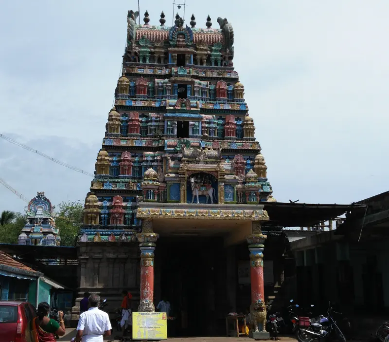 A tall, multi-tiered gopuram painted in many colours, with a doorway and two painted pillars at its base.