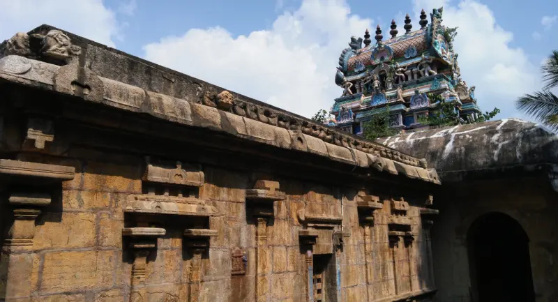 Weathered sandstone wall with carved pilasters, and a colourful tower rising behind it against the sky