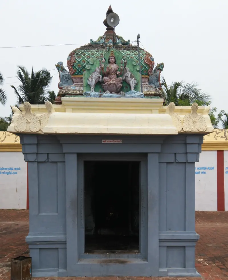 Grey shrine with a dark doorway; a seated goddess flanked by two elephants is on the roof.