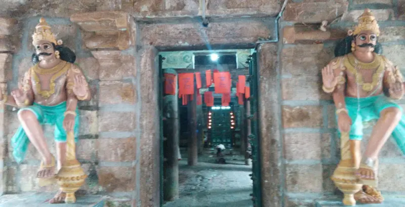 Two seated painted guardian figures flank a doorway with red cloths hanging inside
