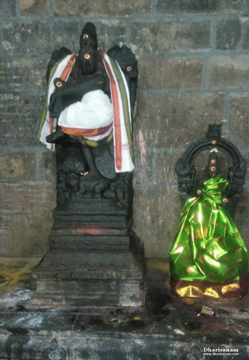 A tall black idol with a white cloth beside a small idol wrapped in shiny green cloth.