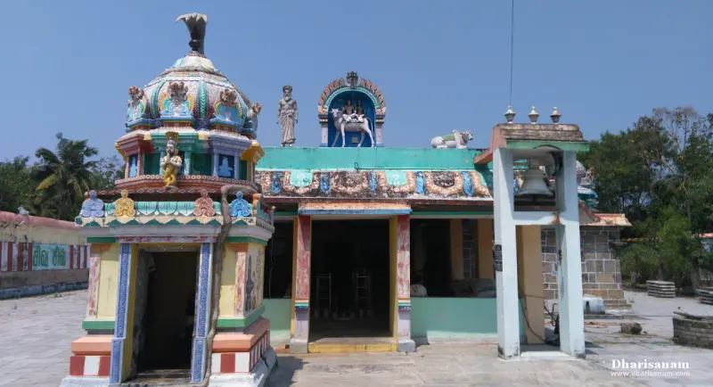 A painted shrine with a domed corner tower, a bull figure and a stucco panel on the roof, and a bell frame in front