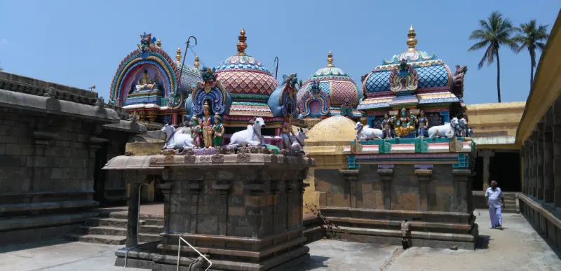 Several painted shrine domes with white bulls above stone bases, around a paved courtyard; a man walks at right