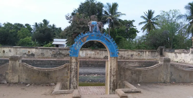 A blue arch stands at the top of steps leading down to a tank, with trees behind