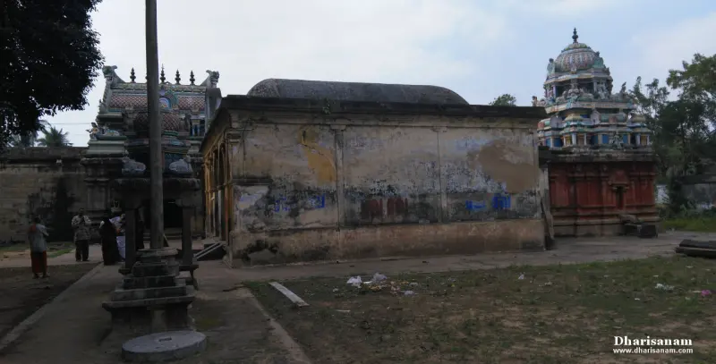A grassy courtyard with a weathered hall under a low dome, a painted tower at right and a stone lamp post base