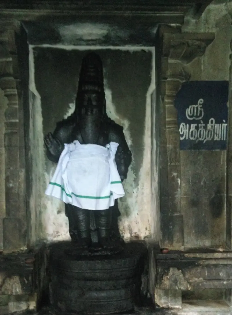 A dark standing figure with a raised hand in a niche, beside a Tamil name board