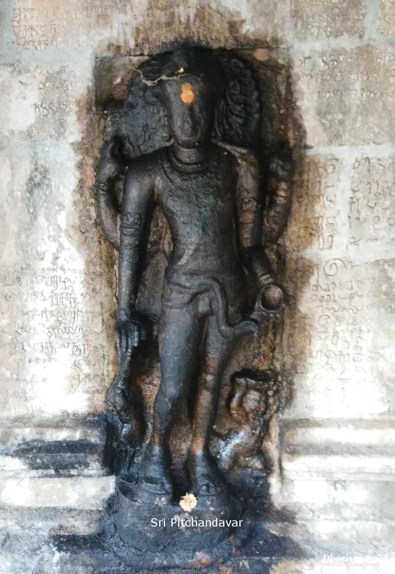 A standing black stone idol in a wall niche, with old Tamil inscriptions on the wall around it