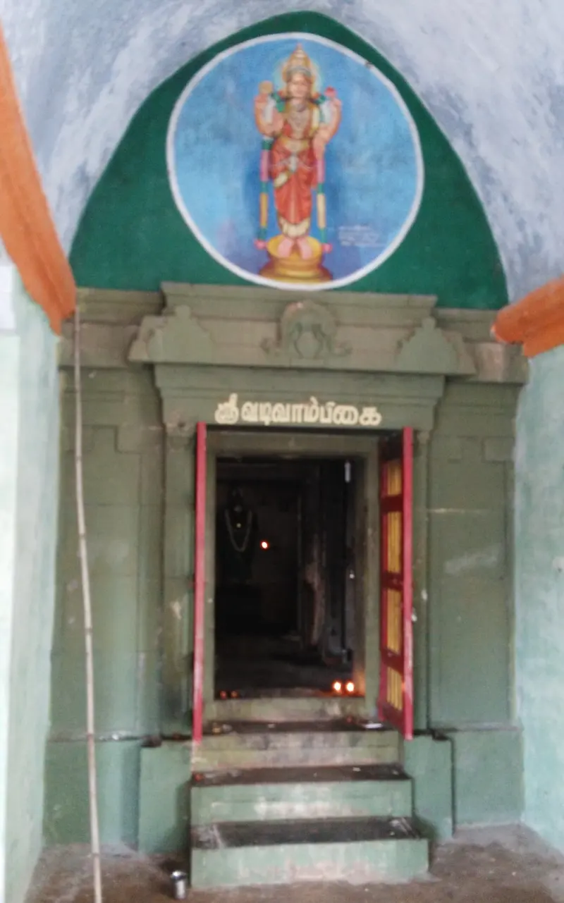 A small shrine doorway with lamps inside and a painted goddess in a round panel above