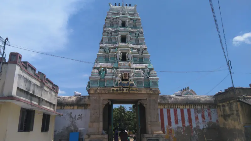 A tiered tower with sculptures above a stone gateway and a wall painted with red stripes