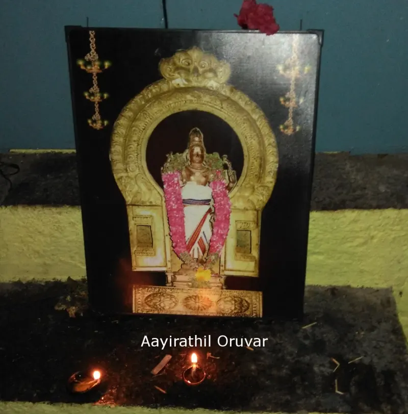 A framed garlanded deity photograph with two oil lamps burning before it