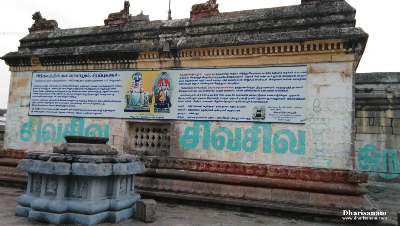 A stone wall with a large painted notice board of text and two deity pictures, and a carved base in front