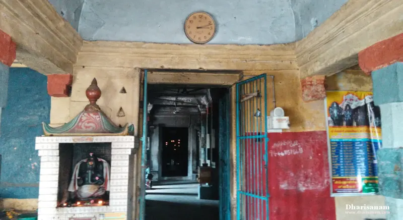 Open blue gate into a corridor, a clock above and a small shrine at left