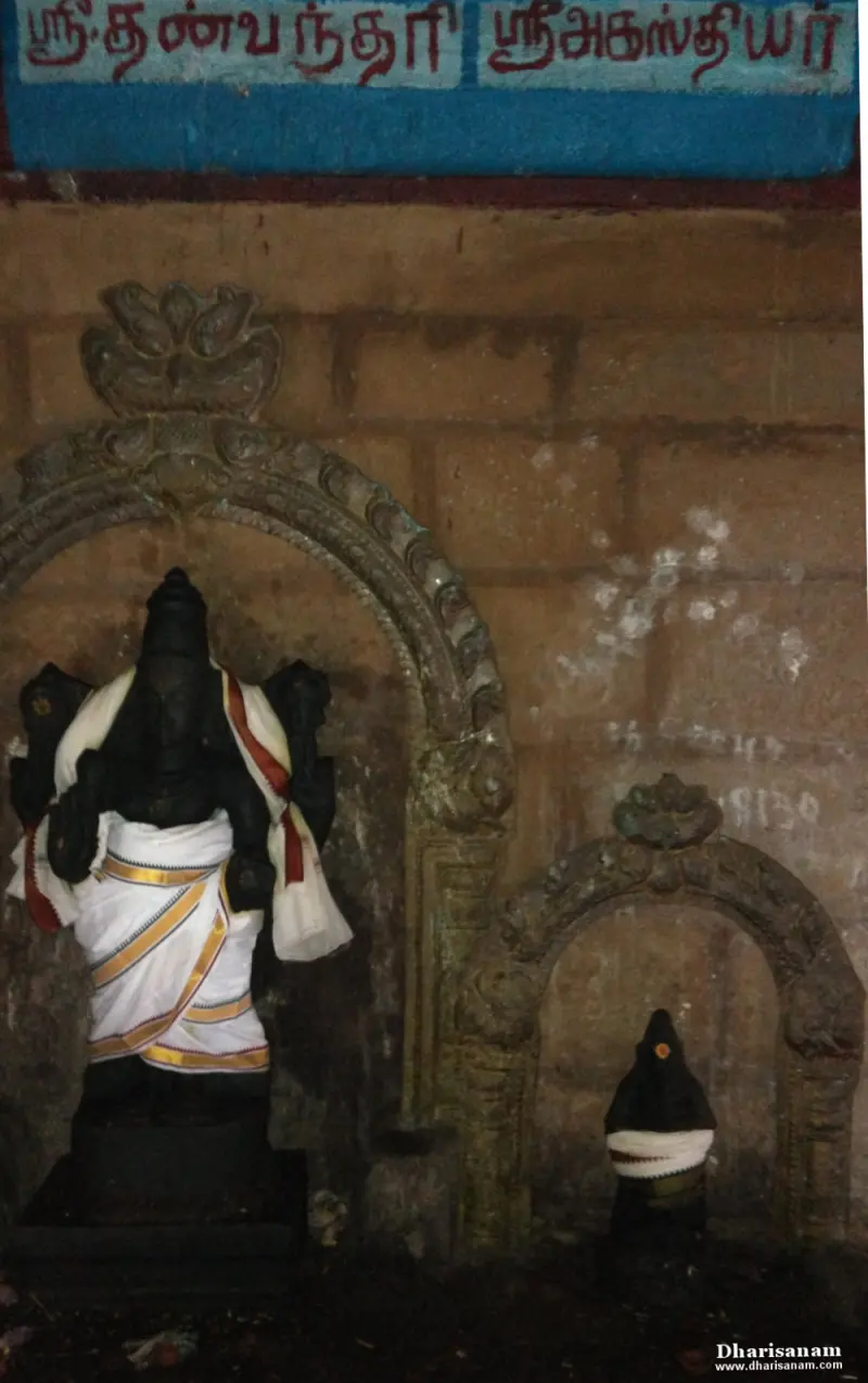 Two dark stone idols in arched wall niches under a blue board with red Tamil lettering