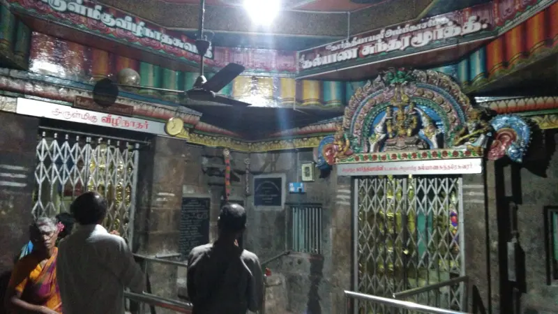 Two grilled shrine doorways with Tamil name boards; the right one has a painted arch above it. Devotees stand at left.