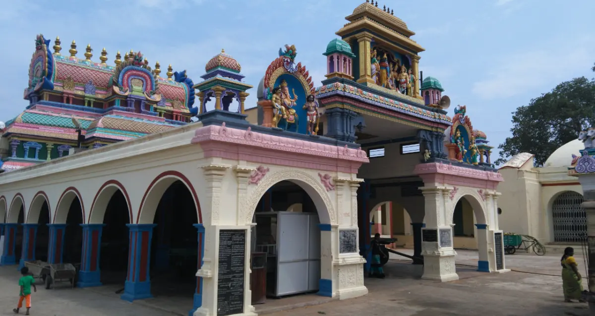 A pillared entrance hall with an arched doorway and painted towers behind, a child and visitors nearby